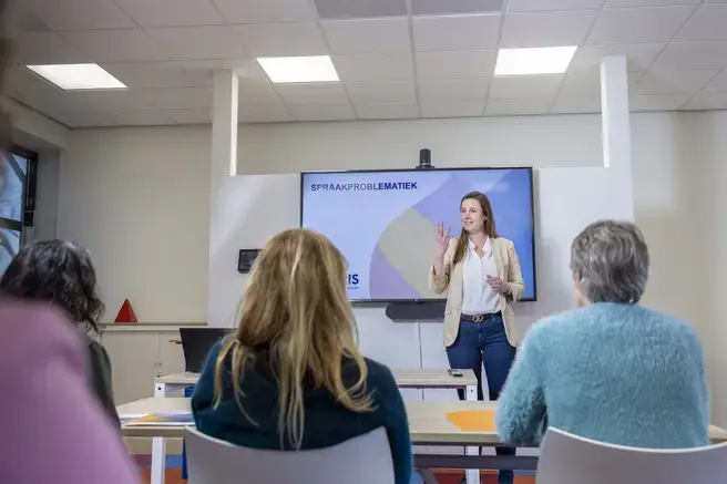 Een vrouw geeft een presentatie over spraakproblematiek voor een groep collega's.